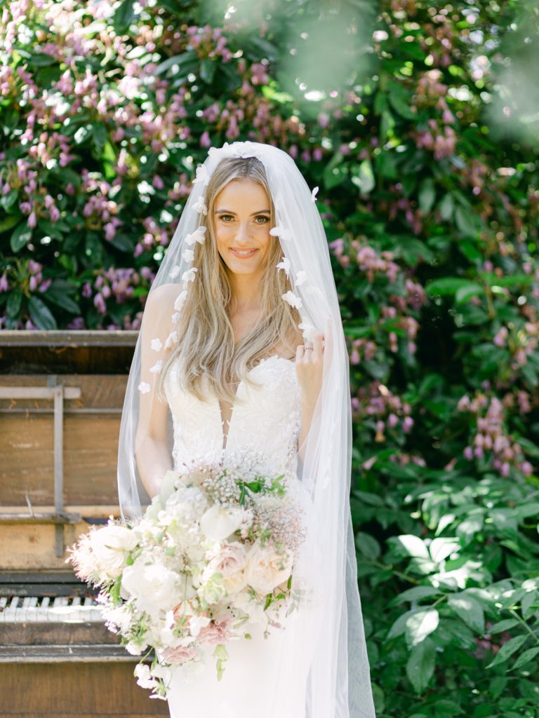 Erin in the gardens with an old piano and greenery as the backdrop.