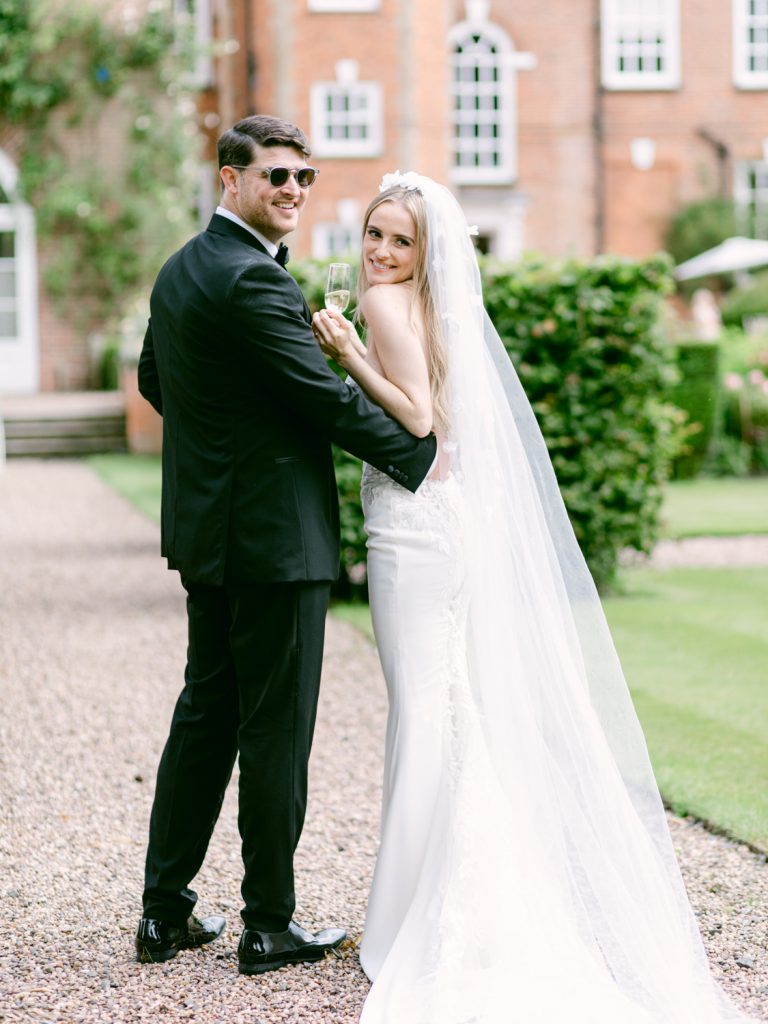 Groom wearing sunglasses and bride carrying champagne, a happy, summery image.