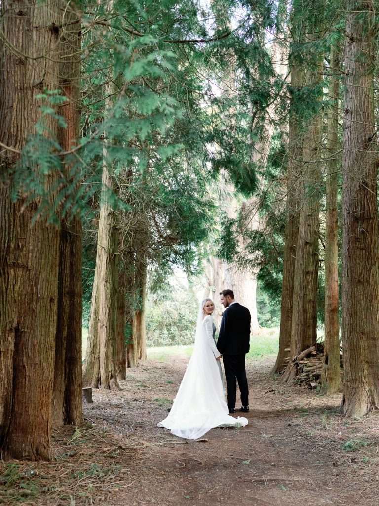 Bride and groom among tall fir trees in the grounds of Hawkstone Hall