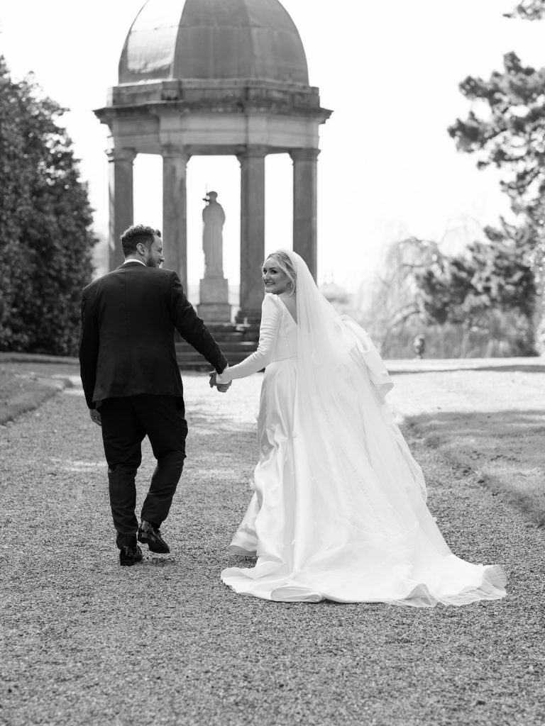 Bride and groom walking hand in hand in the gardens