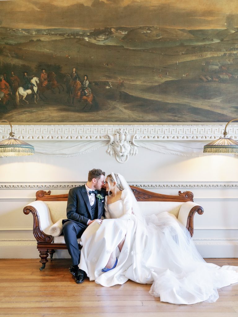 Jess and Lewis sitting together on a couch in the Winter Garden under a large painting