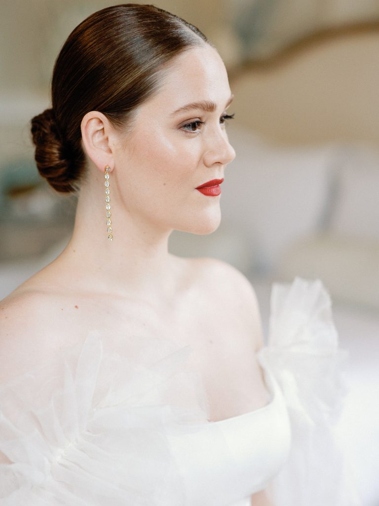Bride Else sitting at the dressing table with natural makeup, stylish up-do and red lipstick.