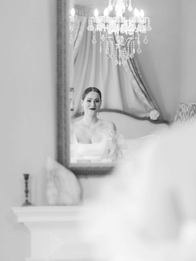 Black and white edit of Else looking through a mirror and smiling before the wedding ceremony.