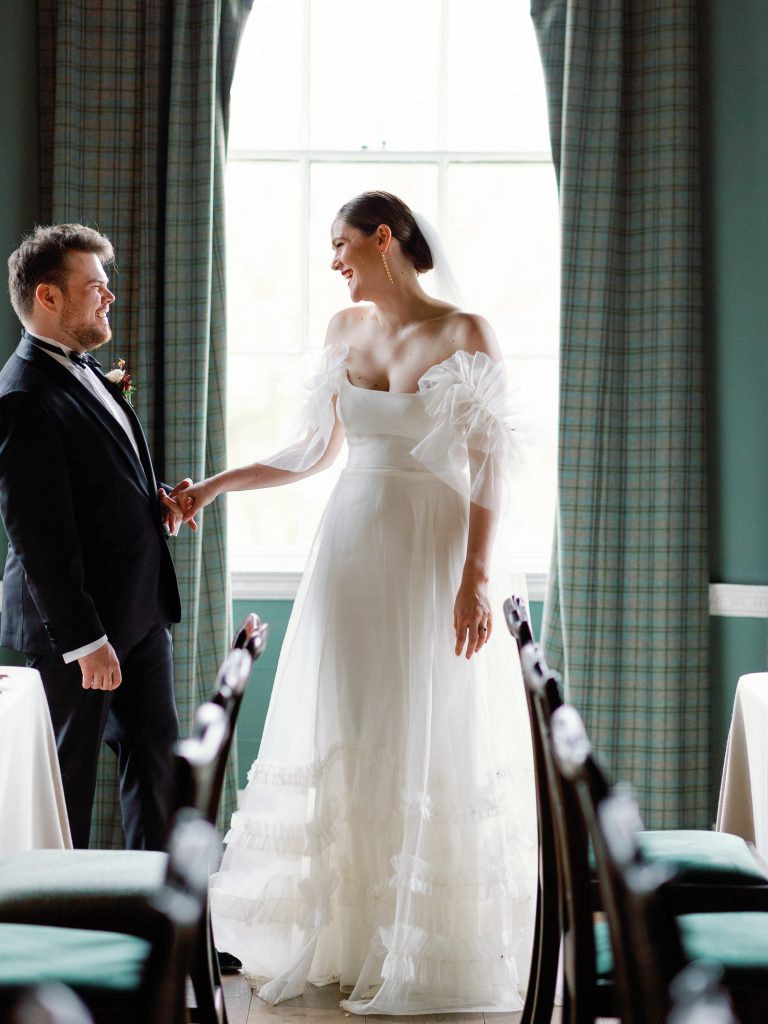 Else and Rory standing facing each other and smiling in the wedding breakfast room before their guests arrive.